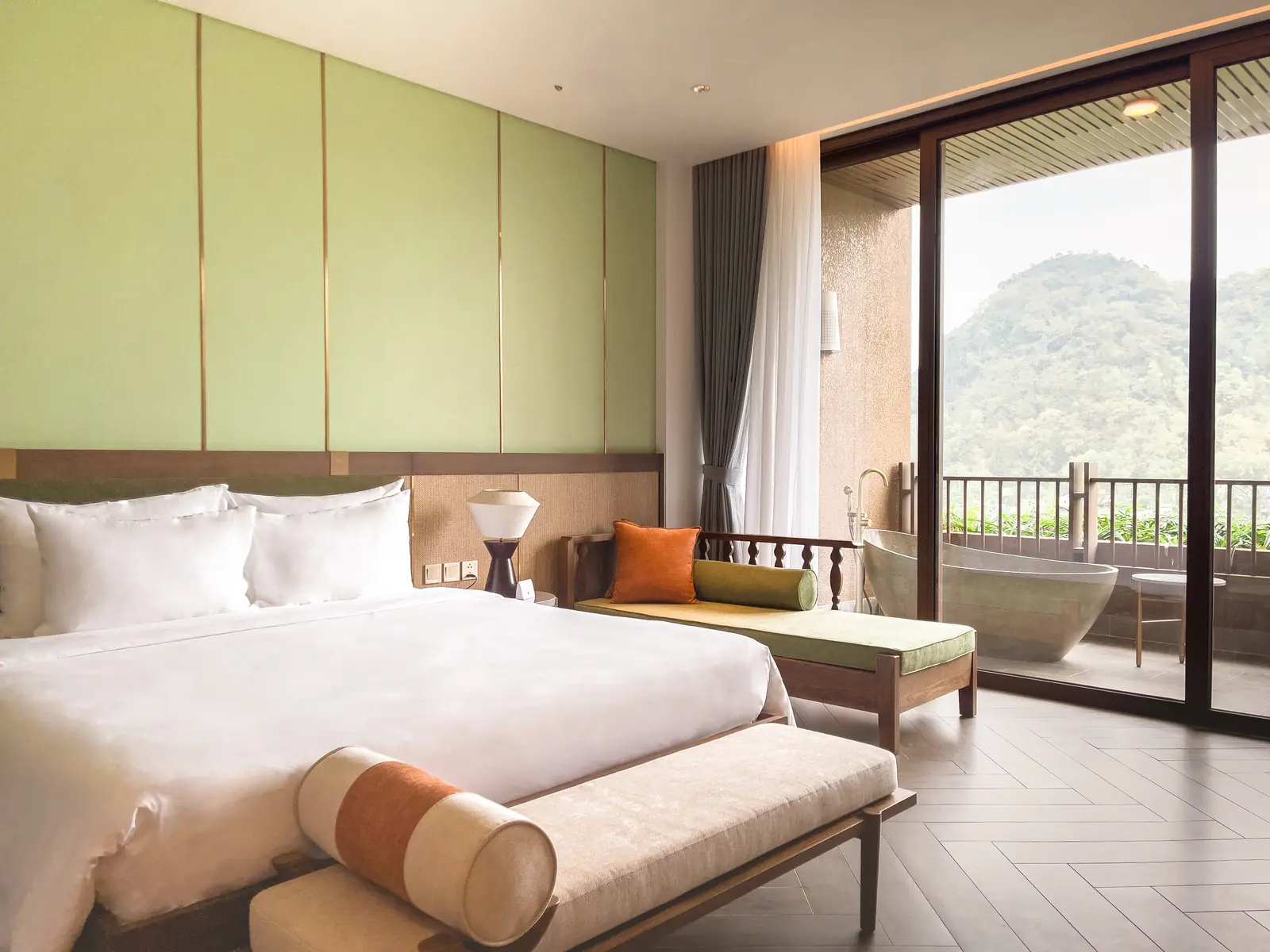 Phòng Family Suite giường đôi trắng, cửa kính mở ra ban công có bồn tắm đá nhìn ra núi xanh