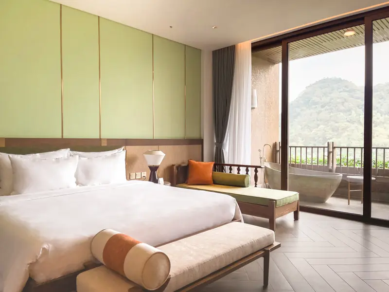 Phòng Family Suite giường đôi trắng, cửa kính mở ra ban công có bồn tắm đá nhìn ra núi xanh