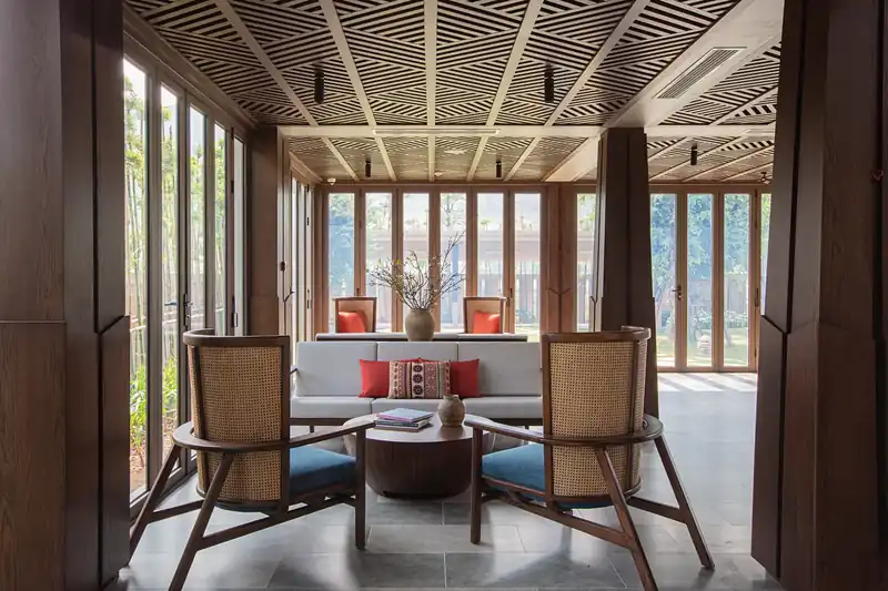 Góc tiếp khách trong nhà đón tiếp, nơi bạn báo mã đặt phòng sau khi chuyển cọc Mandala Kim Bôi: ghế mây đệm xanh, sofa gối đỏ, trần gỗ đan, vách kính nhìn ra vườn