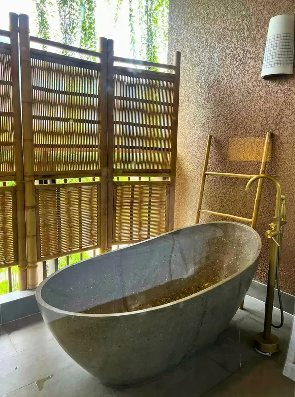 Bồn tắm đá đặt trên ban công phòng nghỉ, vách tre che bên cạnh và giá treo khăn