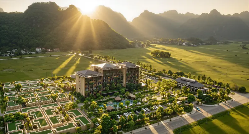 Mandala Retreats Kim Bôi nhìn từ trên cao lúc bình minh: tòa phòng nghỉ, dãy villa và bể bơi giữa cánh đồng lúa, phía sau là núi đá vôi