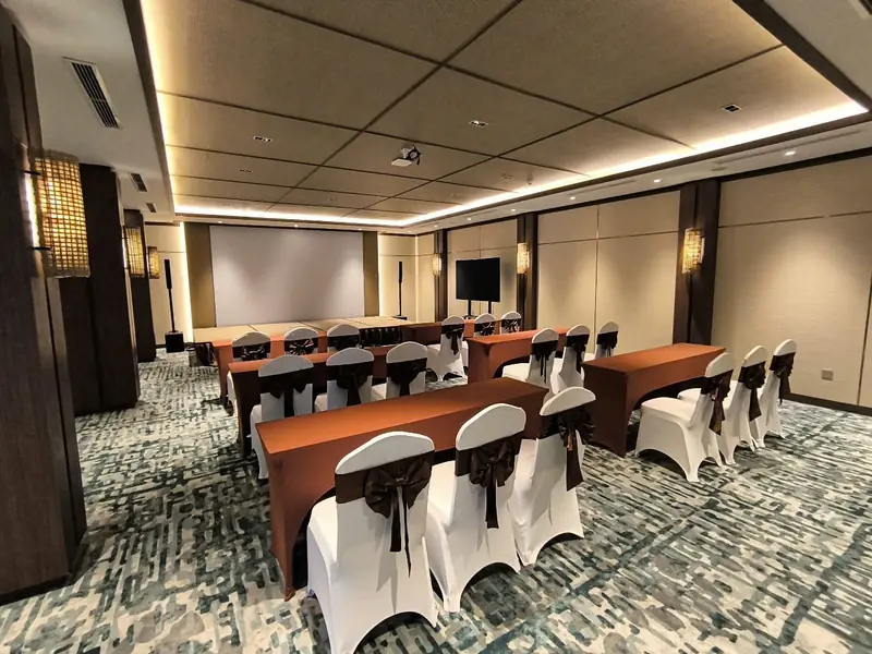 Phòng họp kê bàn khăn nâu kiểu lớp học, ghế bọc trắng, màn chiếu và tivi phía trước
