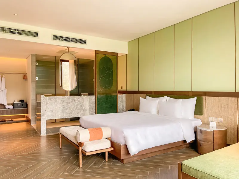 Phòng Master Suite tường xanh nhạt, giường lớn, ghế dài cuối giường và gương tròn