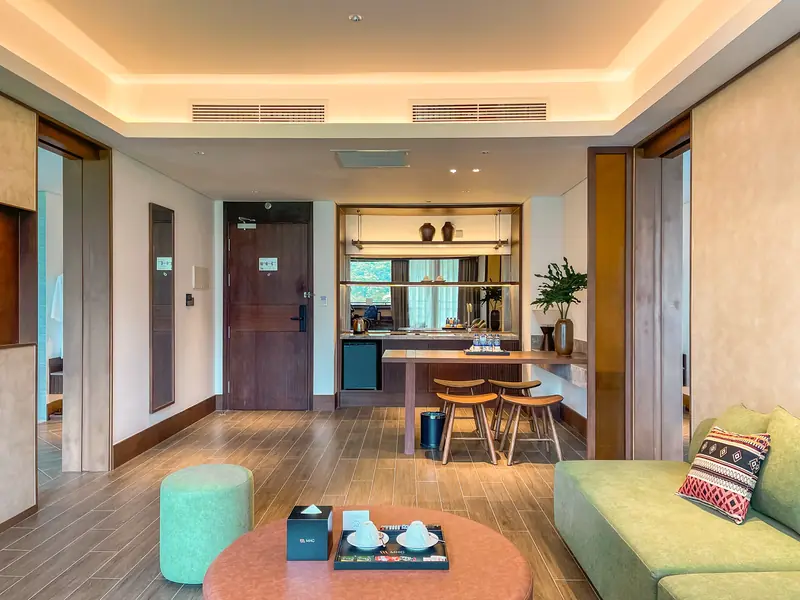 Phòng khách Family Suite: sofa xanh gối thổ cẩm, bàn tròn hồng đất, quầy bar nhỏ và ghế cao