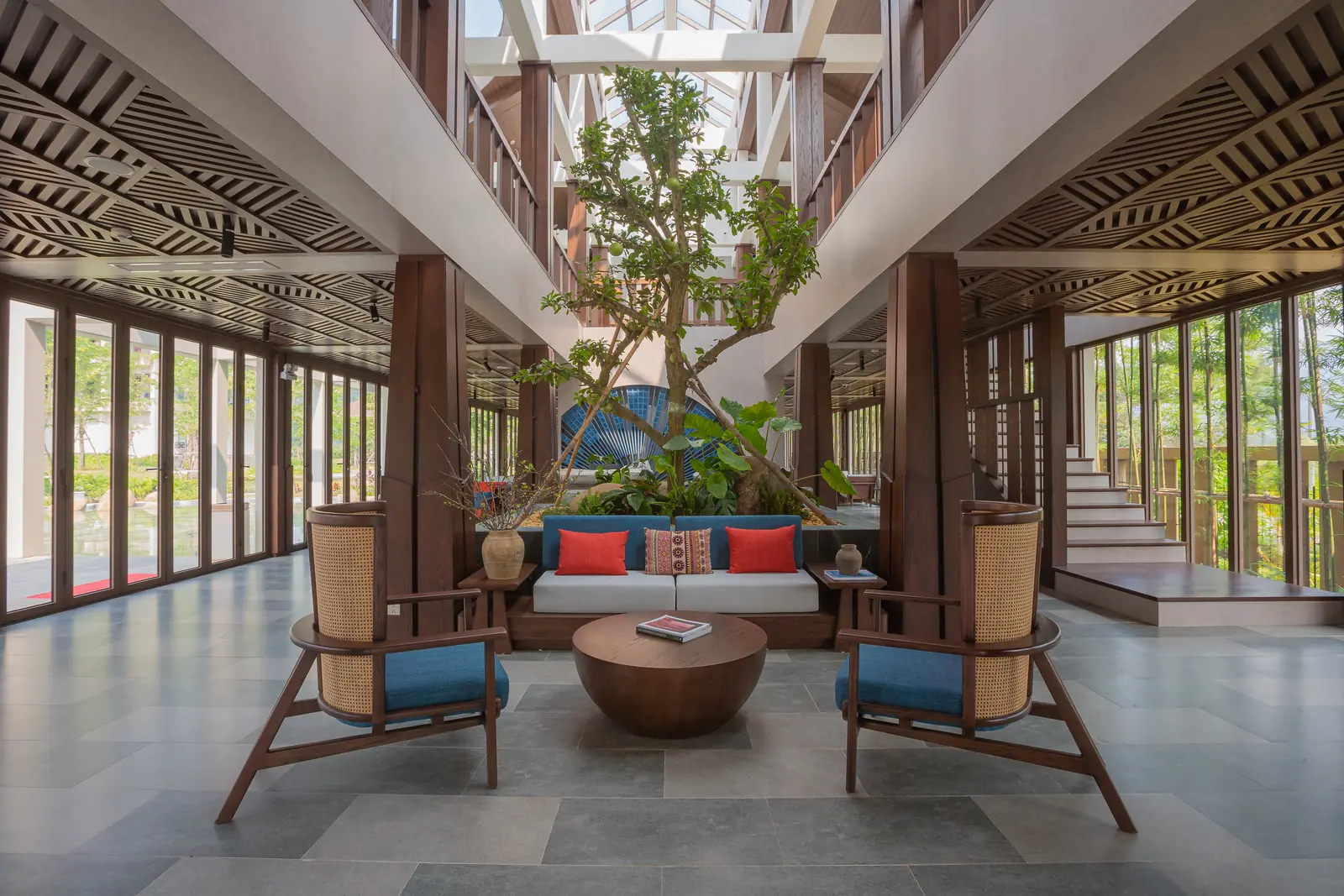Sảnh đón tiếp Mandala Retreats Kim Bôi: giếng trời với cây xanh, sofa gối đỏ, hai ghế mây và trần lam gỗ