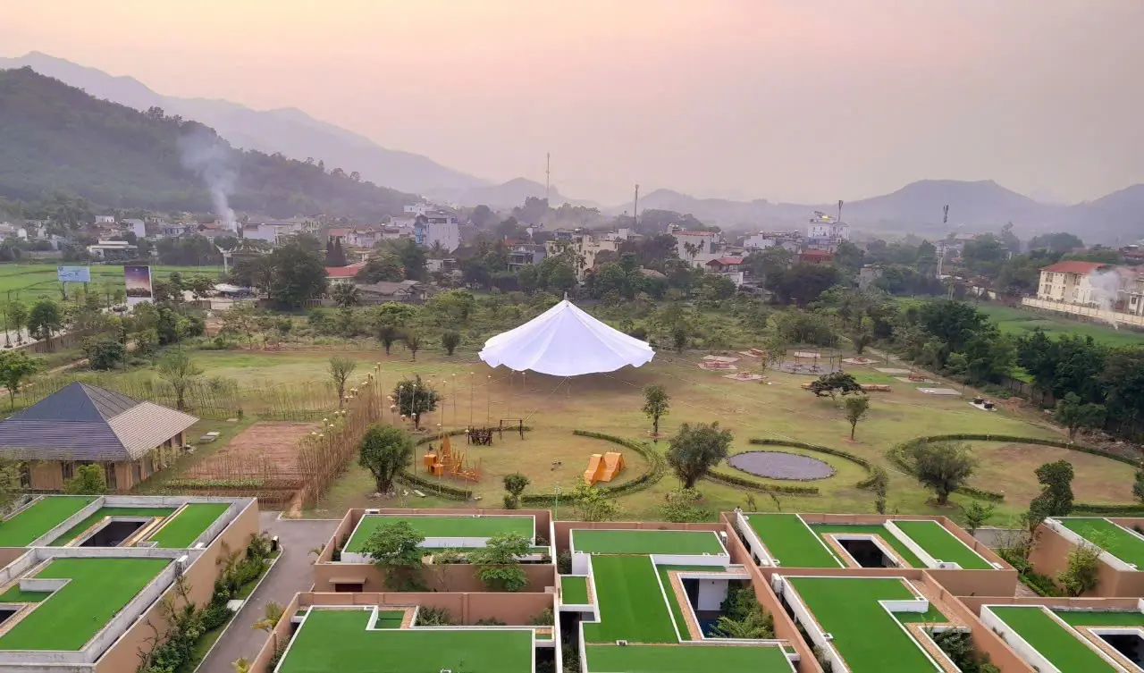 Dãy villa mái phủ cỏ và lều tiệc trắng của Mandala Kim Bôi lúc chạng vạng, xa xa là núi