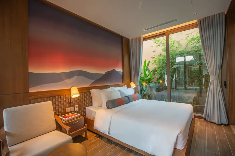 Phòng ngủ villa La Minh: giường đôi, tranh núi đỏ trên đầu giường, ghế bành và cửa kính ra vườn
