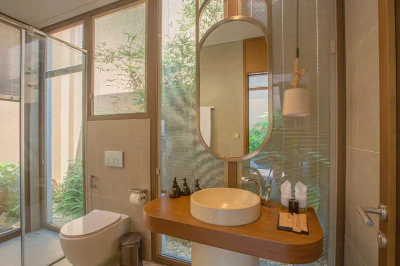 Phòng tắm villa La Sen: lavabo trên bệ gỗ, gương bầu dục, vách kính nhìn ra khóm tre